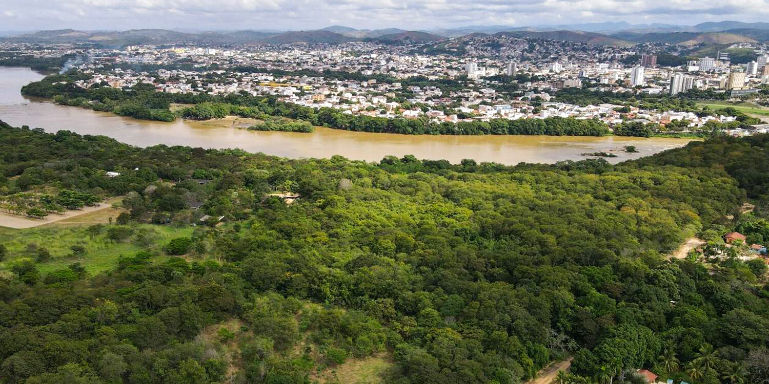 Vista aérea de cidade às margens de um rio, com mata ciliar em primeiro plano
