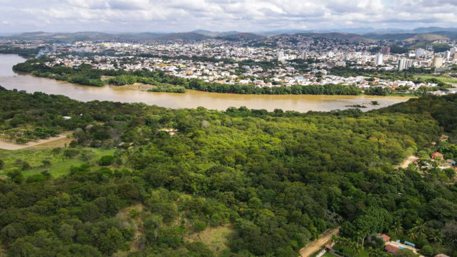 Vista aérea de cidade às margens de um rio, com mata ciliar em primeiro plano