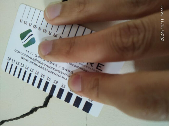 Medição de fissura em parede com fissurômetro durante vistoria técnica