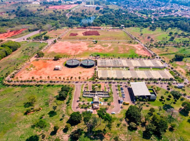 Vista aérea de estação de tratamento de esgoto com tanques circulares e leitos de secagem